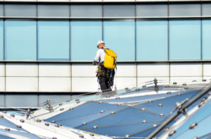 Image of man in safety harness syanding on a glass roof